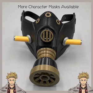 Pode incluir: Uma máscara preta com um filtro central dourado, dois cilindros amarelos horizontais nas laterais e detalhes circulares dourados. O texto "More Character Masks Available" está impresso no topo, com ilustrações de personagens de anime abaixo.