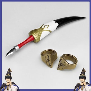 May include: A prop set featuring a curved, horn-shaped object with a white and black finish, a gold-colored band, and a red handle with a silver-toned metal tip. Two matching gold-colored rings with engraved black symbols are positioned nearby.