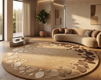 May include: A large, round area rug with a pebble design in shades of beige and brown. The rug is placed on a hardwood floor in a modern living room setting, with a curved sofa and a glass coffee table.