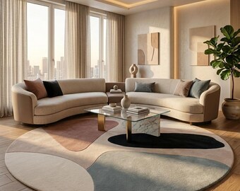 May include: A modern living room featuring two curved beige sofas with accent pillows, a glass-top coffee table, and a large round rug with abstract shapes in neutral colors. A potted plant adds a touch of greenery.