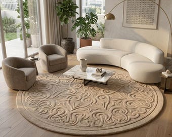 May include: A large, round, beige area rug featuring a raised, intricate, swirling pattern across its surface. The rug is positioned in a living room setting, centered beneath a rectangular marble coffee table, two armchairs, and a curved sofa.