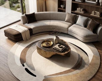 May include: A curved beige sofa with brown and gray throw pillows, a brown ottoman with a white throw blanket, and a round rug featuring abstract concentric circles in shades of cream, tan, and brown, centered by a low-profile organic wood coffee table.