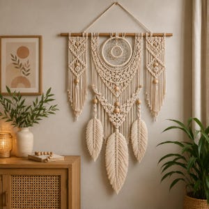 May include: A large cream-colored macrame wall hanging suspended from a wooden rod. The design features intricate knotted patterns, a central circular dreamcatcher element, wooden beads, and three large, fringed leaf-shaped tassels.