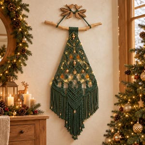 Può includere: Una decorazione da parete in macramè verde scuro a forma di albero di Natale, appesa a un ramo di legno. Presenta complessi motivi a nodi, perline dorate, ornamenti a forma di stella, luci calde e un motivo con uccellini in legno in cima.