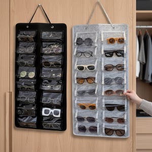Peut inclure: Deux organisateurs de lunettes suspendus, un noir et un gris, chacun avec plusieurs poches transparentes contenant diverses paires de lunettes et de lunettes de soleil. Les organisateurs sont suspendus à des crochets, présentant une solution de rangement pratique pour les lunettes.
