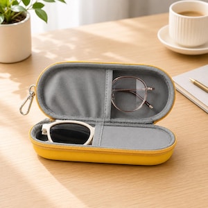 Pode incluir: Um estojo rígido para óculos de formato oval, na cor amarelo brilhante, com fecho de correr e um mosquetão prateado. O interior é forrado com tecido cinzento macio e possui um divisor central, contendo óculos de grau e óculos de sol.