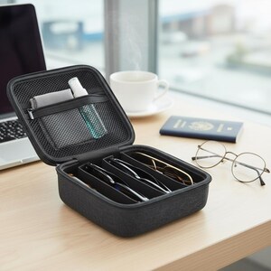 Puede incluir: Un estuche negro para gafas con varios compartimentos, abierto para revelar varios pares de gafas. El estuche también contiene un paño de limpieza y un pulverizador. Una computadora portátil, un pasaporte y una taza de café están cerca.