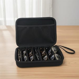Könnte beinhalten: Geöffnete schwarze Sonnenbrillenetui mit mehreren Fächern, in denen verschiedene Sonnenbrillenpaare ausgestellt sind. Das Etui hat eine Netztasche und einen Griff. Die Sonnenbrillen sind in verschiedenen Stilen und Farben.