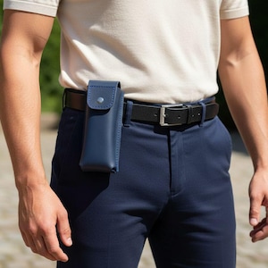 May include: A navy blue leather case attached to a black belt. The case has a flap secured by a snap. The person is wearing a light-colored shirt and navy blue pants. The belt has a silver buckle.