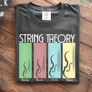 May include: A black t-shirt featuring the text "STRING THEORY" in white. Underneath, four vertical rectangles display violin illustrations and the names "Violin", "Viola", "Cello", and "Bass" in green, mauve, blue, and yellow.