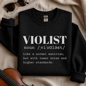 May include: A black crewneck sweatshirt featuring white text that reads VIOLIST noun /vi'ouləst/ Like a normal musician, but with lower notes and higher standards. The garment has long sleeves and a ribbed collar, cuffs, and hem, with a visible brand label.