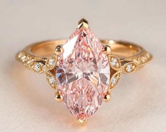 May include: A gold ring featuring a large marquise-cut light pink center stone held by prongs. The band is crafted from yellow gold with intricate milgrain detailing and small round accent diamonds set along the shoulders of the ring setting.