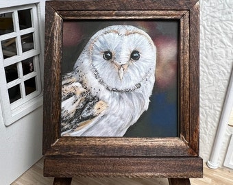 May include: A framed painting of a barn owl with a white face and brown and white feathers. The painting is on a dark brown easel.