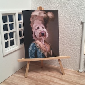 May include: A painting of a dog wearing a gold and white hat and a blue and green dress. The dog is looking directly at the viewer. The painting is on an easel.