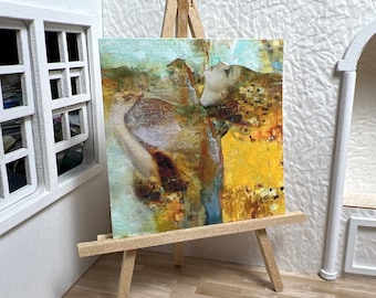 May include: A painting on a wooden easel with a colorful abstract design featuring a woman's face and a yellow and blue background.