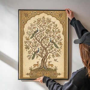 May include: A rectangular framed wall art print featuring a central tree with three peacocks perched on branches and two deer standing at the base. The illustration is set against a cream background with an ornate gold border in a pointed arch shape.