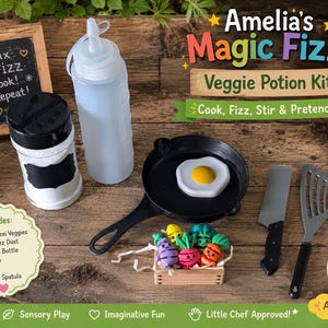 Pode incluir: Um conjunto de cozinha de brinquedo rotulado Amelia's Magic Fizz Veggie Potion Kit, incluindo uma mini frigideira preta com um ovo frito de plástico, uma garrafa de apertar, um agitador, uma faca, uma espátula e uma caixa de madeira com cinco mini vegetais.