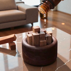 Op de afbeelding: Een donkerbruine houten kom gevuld met kleine, vierkante houten blokken. Een bruine glazen fles giet een heldere vloeistof op de blokken. De kom staat op een lichtgekleurd, gespikkeld oppervlak, met een bruine bank op de achtergrond.