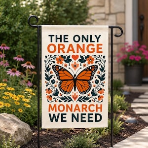 Può includere: Una bandiera da giardino rettangolare con sfondo color crema, un'illustrazione centrale di una farfalla monarca arancione e nera circondata da motivi floreali verde scuro. Il testo recita THE ONLY ORANGE MONARCH WE NEED in arancione e verde scuro.