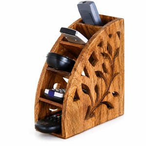 May include: A wooden remote control organizer with a carved floral design. The organizer has multiple compartments holding various remote controls. The wood has a warm, natural finish, and the design includes leaf-shaped cutouts.