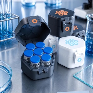 May include: A hexagonal 10 mL vial case with a hinged lid and latch, available in black or white. The case holds seven small glass vials with blue caps. The lid features a hexagonal logo, and a label reads 10 mL VIAL CASE.