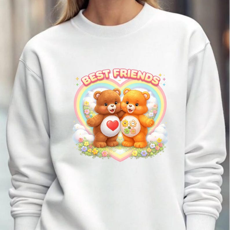 May include: White sweatshirt featuring a graphic of two teddy bears hugging, with a heart and flower design. The words "BEST FRIENDS" are arched above the bears in a colorful font, set against a rainbow heart.