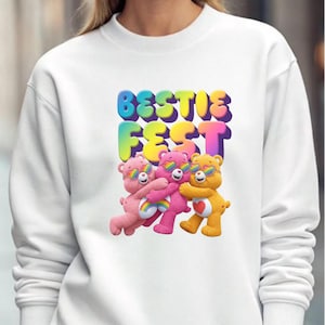 May include: White sweatshirt featuring the text "BESTIE FEST" in colorful bubble letters above three cartoon bears wearing sunglasses. The bears are pink, magenta, and yellow, with rainbow accents.