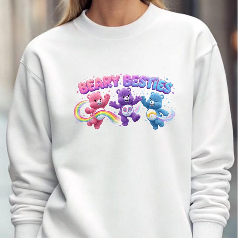 May include: White sweatshirt featuring the phrase "BEARY BESTIES" above three cartoon bears in pink, purple, and blue. The bears are positioned above a rainbow and a trail of sparkles.