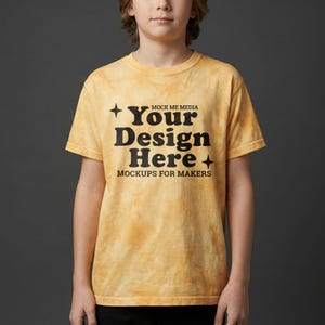 May include: A yellow tie-dye t-shirt with the text "Your Design Here" in a bold, black font. The shirt also includes the text "Mockups for Makers" and "Mock Me Media". The shirt is short-sleeved.