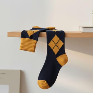 May include: Navy blue socks with a mustard yellow diamond pattern. The socks have mustard yellow heels and cuffs. The socks are displayed on a wooden shelf against a white background.