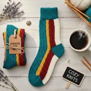 May include: A pair of handmade knit socks with a teal cuff and toe, and a white foot. The socks feature vertical stripes in red, yellow, and teal. A tag reads "Handmade with Love". A sign says "Cozy Knits".