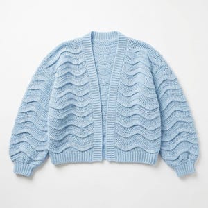 Puede incluir: Un cárdigan azul claro con frente abierto y un patrón de ganchillo ondulado. El suéter de manga larga tiene un ajuste relajado y puños y dobladillo acanalados. El color azul suave y el diseño texturizado crean un aspecto acogedor y elegante.