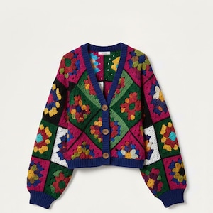 Puede incluir: Un cárdigan de ganchillo colorido con un diseño de patchwork. El suéter presenta un cuello en V, cierre de botones y mangas largas. La paleta de colores incluye tonos de rosa, verde, azul, amarillo y negro. Los puños y el cuello son de color azul marino liso.