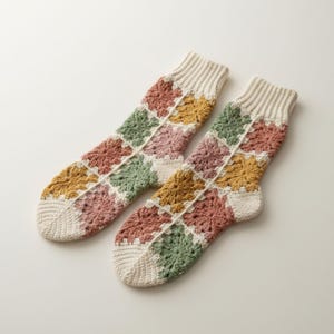 May include: A pair of handmade crochet socks. The socks feature a patchwork design with squares of various colors, including green, pink, yellow, and cream. The cuffs and toes are cream-colored.