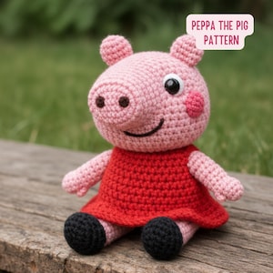 May include: A handmade Peppa Pig crochet doll. The pig is pink with a red dress and black shoes. The text "Peppa the Pig Pattern" is in a white bubble. The doll is sitting on a wooden surface against a blurred green background.