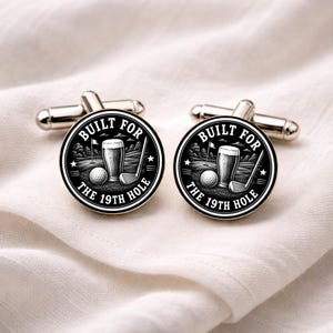 May include: Silver cufflinks with a golf-themed design in black and white. Each cufflink has a circular emblem with the text "BUILT FOR THE 19TH HOLE" around a golf ball, club, pint of beer, and flag.