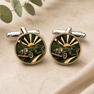 May include: A pair of round silver-toned cufflinks featuring a detailed illustration of a vintage green car driving on a road. The background displays a stylised sunburst pattern in shades of dark green, black, and cream, set against a metallic frame.