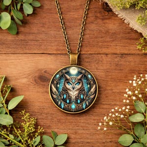 Op de afbeelding: Een bronzen hangerketting met een gedetailleerd uilontwerp. De uil heeft blauwe ogen en staat tegen een teal en witte achtergrond met een volle maan. De hanger hangt aan een bijpassende ketting.