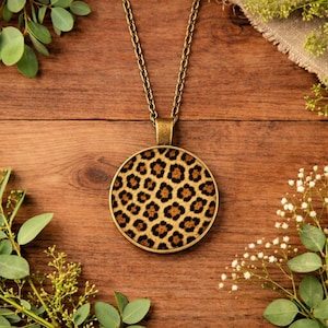 May include: A gold-toned pendant necklace with a round leopard print design. The pendant hangs from a matching chain, creating a stylish accessory. The leopard print features brown spots on a tan background.