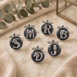 May include: Six round silver-toned cufflinks featuring a dark grey recessed background. Each cufflink displays a raised silver letter—S, M, R, B, J, or D—integrated with a detailed wolf head profile design. The cufflinks have a standard T-bar closure.