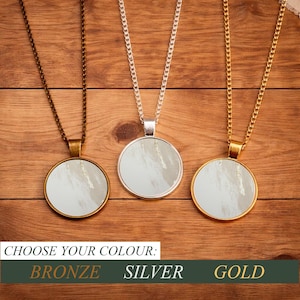 May include: Three pendant necklaces with circular, abstract art designs. The necklaces are bronze, silver, and gold. The text at the bottom reads "CHOOSE YOUR COLOUR: BRONZE SILVER GOLD."