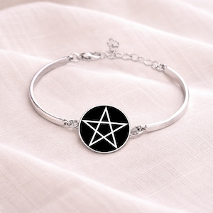 May include: Silver-toned bracelet featuring a black circular pendant with a white pentagram design. The bracelet has a simple, elegant design with a delicate chain for adjusting the size. The bracelet is displayed on a soft, light-colored fabric.