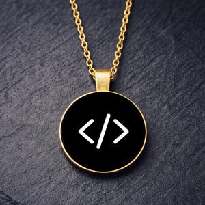 Peut inclure: Un collier doré avec un pendentif rond. Le pendentif présente un fond noir et un symbole de code blanc. La chaîne est dorée et le pendentif a une bordure dorée. Le collier est posé sur une surface sombre et texturée.