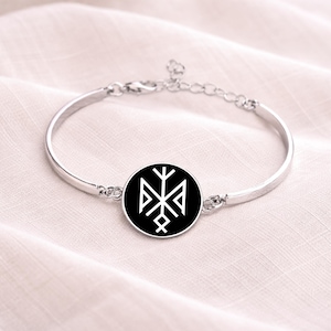 May include: A silver-toned bangle bracelet featuring a circular black pendant with a white geometric design. The bracelet has a simple, elegant design with an adjustable chain closure. The pendant's design is a symmetrical, stylized symbol.