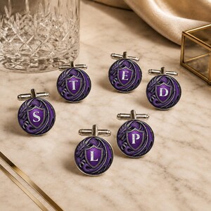 May include: Five circular silver cufflinks featuring a purple dragon motif surrounding a central shield. Each shield displays a single white letter: S, T, E, D, or L. The cufflinks have a polished metallic finish and a standard hinged toggle backing.