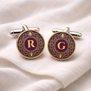 May include: A pair of Art Deco style cufflinks with a purple and gold design. Each cufflink features a circular face with a gold letter, one with an "R" and the other with a "G". The cufflinks have a silver-tone metal backing.