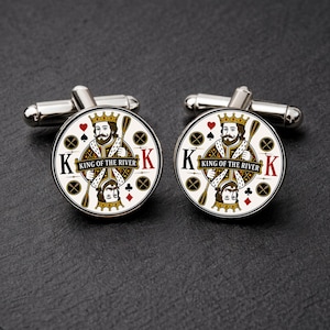 May include: A pair of round silver-tone cufflinks featuring a playing card design. The center displays a king figure holding a paddle with the text KING OF THE RIVER. The background includes card suit symbols and the letter K in black and red.