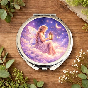 May include: A silver compact mirror with a fantasy scene. It features a fairy with long hair, holding a lantern, seated on clouds under a starry sky with a crescent moon. The mirror is round.