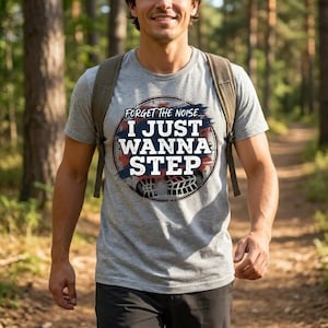 May include: A light gray t-shirt with the text "FORGET THE NOISE... I JUST WANNA STEP" in a circular design. The design includes blue, white, and red accents, with a footprint graphic at the bottom. The person is wearing a backpack.