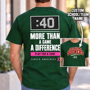 May include: A dark green t-shirt featuring a back graphic with a digital clock display showing :40, the text MORE THAN A GAME A DIFFERENCE, and a pink ribbon icon. An inset shows the front of the shirt with the text OKLAHOMA SOONERS and :40.